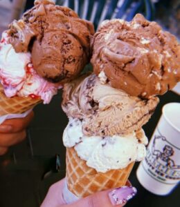 Two Ice Cream cones one with 3 scoops of ice cream and one with two scoops.