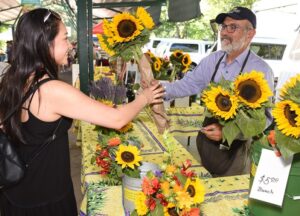 Man handing sunflowers to a young woman at the Davis Farms Market. Both are smiling