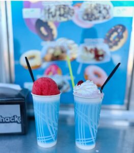 Two cups of shave ice, background is an image of the food trucks but it's blurred