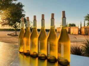 6 bottle of Chardonay on a table at sunset featuring the winery in the background